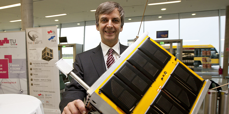 A man holds a model of a satellite into the camera.