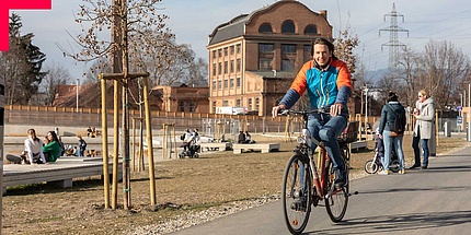 Mann am Fahrrad fährt durch belebten Park