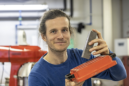 Smiling man with cuboid gray object in hand.