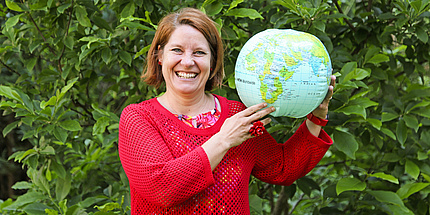 Eine lächelnde Frau in rotem Pullover hält einen aufblasbaren Globus in den Händen.