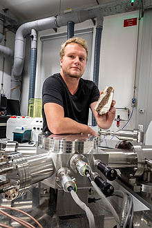 TU Graz researcher with rock sample in front of a mass spectrometer