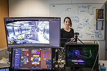 Eine Frau sthet hinter Bildschirmen, auf denen virtuelle Arbeitsumgebungen zu sehen sind.