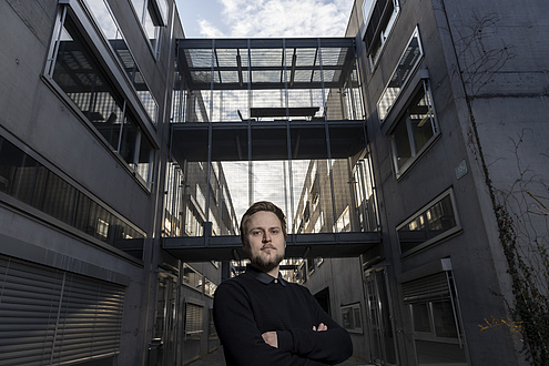 A man stands in front of a building and smiles into the camera