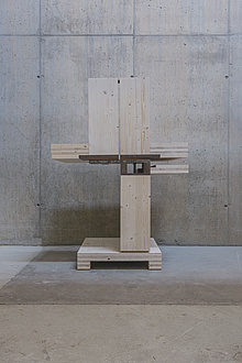 A construction of three wooden parts, one at the bottom and two on top. It looks as if a wooden part is missing at the bottom.
