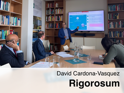 David Cardona-Vasquez präsentiert beim Rigorosum vor drei Gutachtern in einem Bibliotheksraum, zeigt auf eine Folie zu „Planning for Net-zero Energy Systems“ mit Glaskaraffen und Notizen auf dem Tisch.