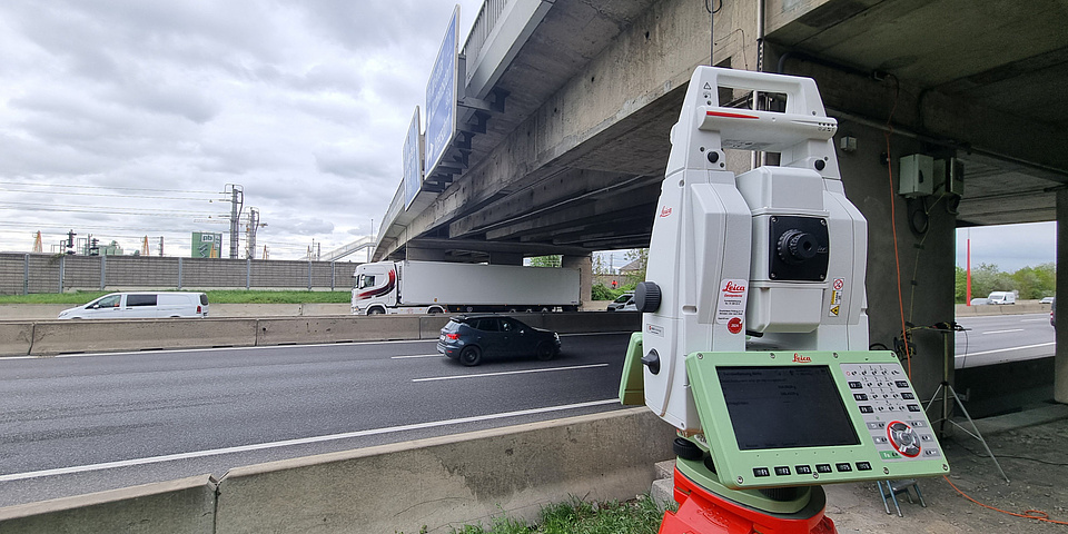 A surveying device stands in front of a motorway bridge.