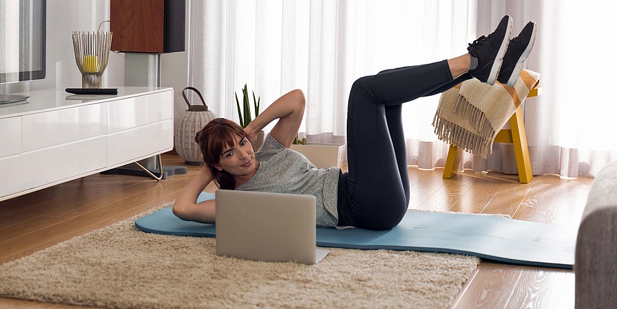 Frau auf Turnmatte beim Training mit Laptop.