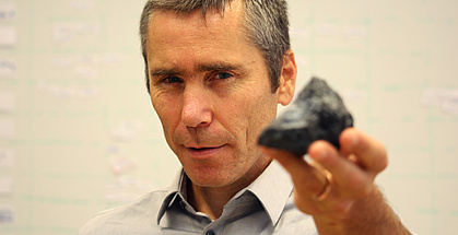 Roman Marte hält einen schwarzen, kantigen Stein in die Kamera.
