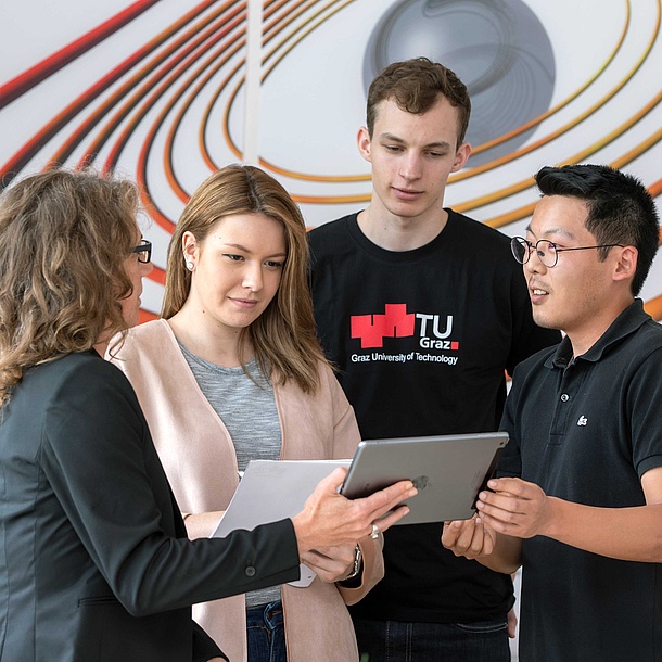 4 people looking at a tablet, one wearing a TU Graz t-shirts