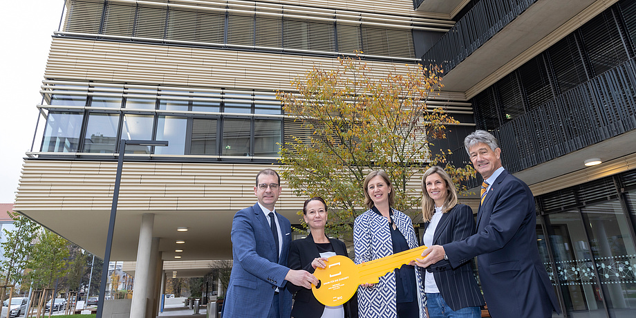 Group photo with three women and two men and an oversized symbolic key