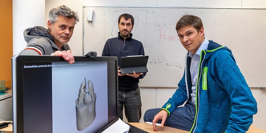 Three scientists in front of a computer screen, a digital heart is depicted