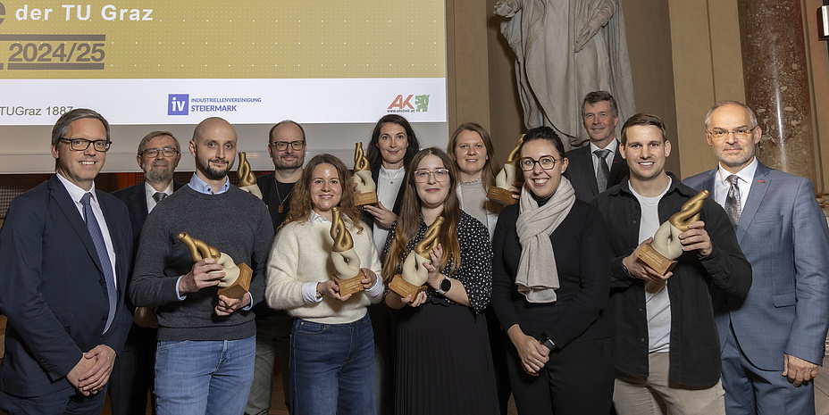 Zwölf Menschen stehen nebeneinnander vor einem Bildschirm und einer Statue.