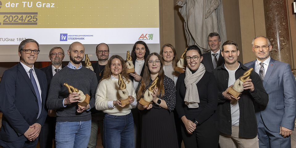Zwölf Menschen stehen nebeneinnander vor einem Bildschirm und einer Statue.