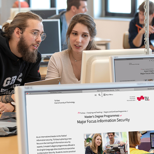 Two students in front of a computer are talking to each other.