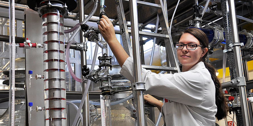 A young woman wearing a lab coat is grabing laboratory pipes.