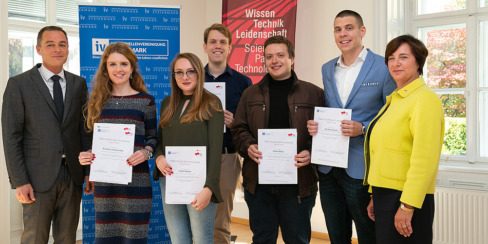 Eine Gruppe von fünf Stipendiatinnen und Stipendiaten halten ihre Stipendien-Zertifikate in die Kamera und sind flankiert von Vertreter/innen der Förderer. 