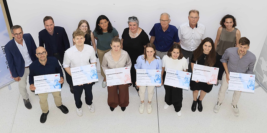 Gruppenbild von 15 Personen von einer Preisverleihung. Die sieben Personen in der ersten Reihe halten ein Zertifikat in den Händen und lächeln freudig in die Kamera. 