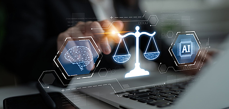 Eine Person tippt auf der Tatsatur eines Laptops, über dem ein Hologramm ischwebt, das eine Waage, ein Gehirn und einen Mikrochip darstellt.