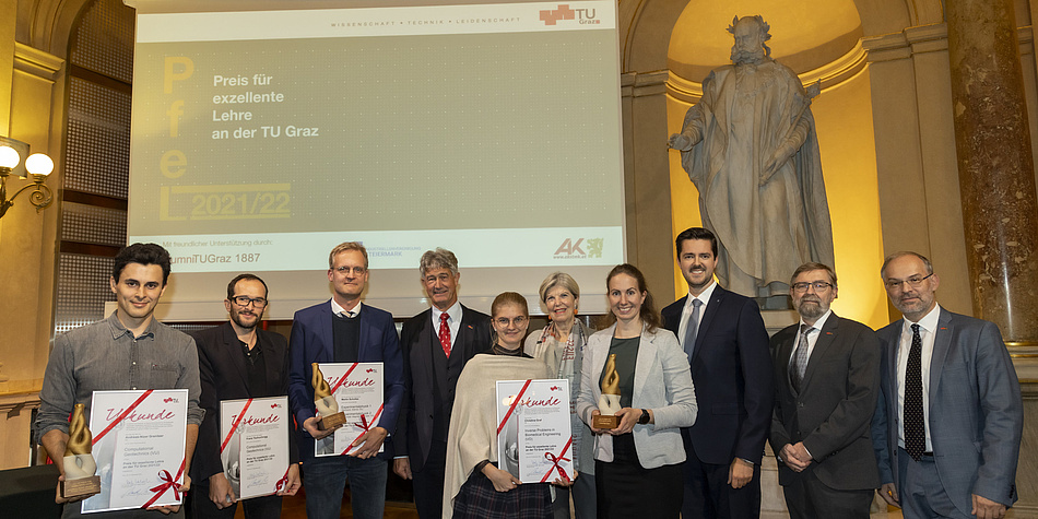 10 smiling people stand in front of a screen on which "Price for excellent teaching" is projected in German. Four people hold a winner's certificate, one holds a trophy.