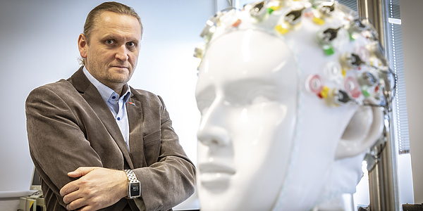 Lächelnder Mann hinter einer Keramikfigur in Form eines menschlichen Kopfes