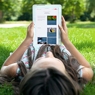 Eine junge Frau liegt im Gras und betrachtet auf ihrem Tablet eine Seite der TU Graz. Bildquelle: BillionPhotos.com – Fotolia.com