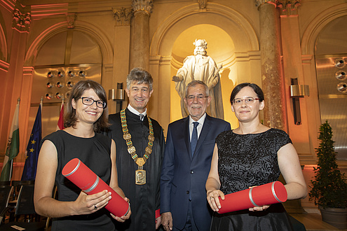 Zwei Frauen und zwei Männer stehen nebeneinander, die beiden Frauen halten rote Rollen in der Hand.