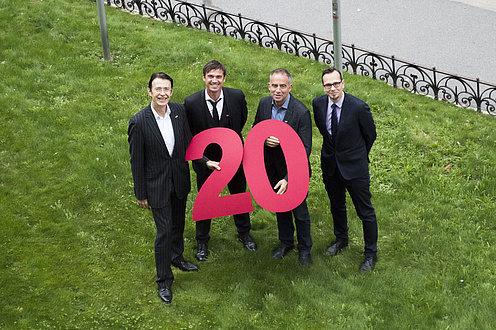 Four men holding big red figures saying "2" and "0".