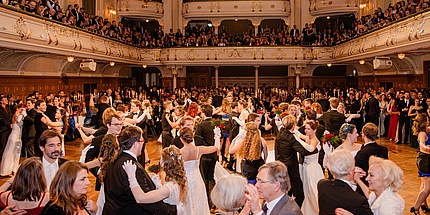 Zahlreiche tanzende Personen in einem festlich geschmückten Ballsaal.