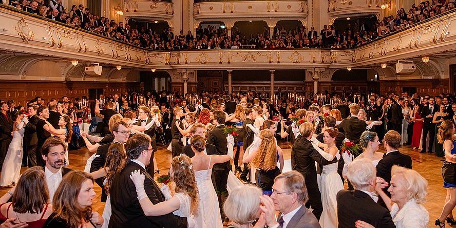 Numerous dancing people in a festively decorated ballroom.