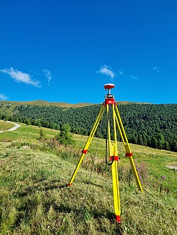 A GNSS antenna stands on a meadow against a blue sky.