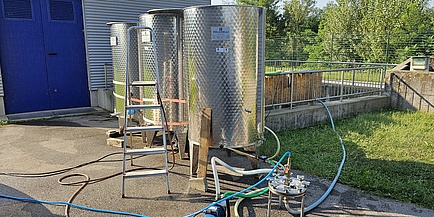 Three steel containers with hoses leading into them. A ladder stands at an angle in front of them.