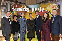 Drei Frauen und vier Männer blicken in die Kamera. Im Hintergrund steht ein Plakat mit dem Titel: Smarty party.