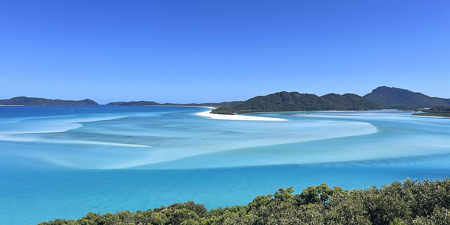 Light blue sea, with wooded hills on the shore behind.