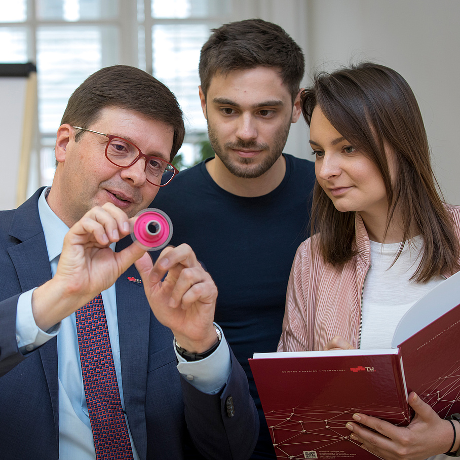 Two men and a woman look at a small, round object.