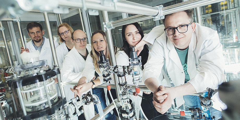 Six researchers in lab coats are leaning against a construction of metal rods in a lab at TU Graz.