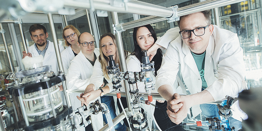 Six researchers in lab coats are leaning against a construction of metal rods in a lab at TU Graz.