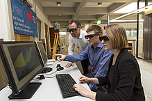 Two men and a woman with special glasses in front of screens.