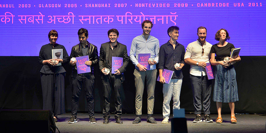 2 junge Frauen und 5 junge Männer unterschiedlicher Nationalitäten bei der Verleihung des Archiprix mit Urkunden vor einer violetten Wand mit der Aufschrift "World's best graduation projects. Ahmedabad 2017".