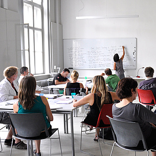 Lecture room with people and a lecturer writing on a black board. Photo source: TU Graz