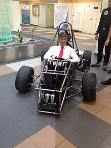 Man with dark hair, white shirt and red tie sits in a racing car.