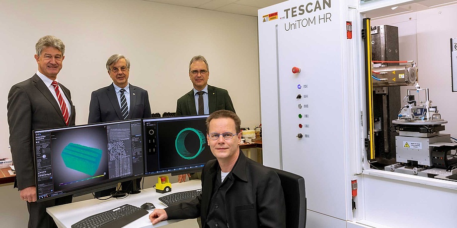 Four gentlemen next to two computer screens and a micro-CT chamber