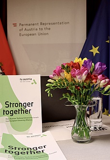 Ein Strauß Blumen steht auf einem Tisch neben einem aufgestellten Flyer.