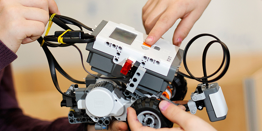 Zwei Kinderhände halten einen selbstgebauten kleinen Roboter.