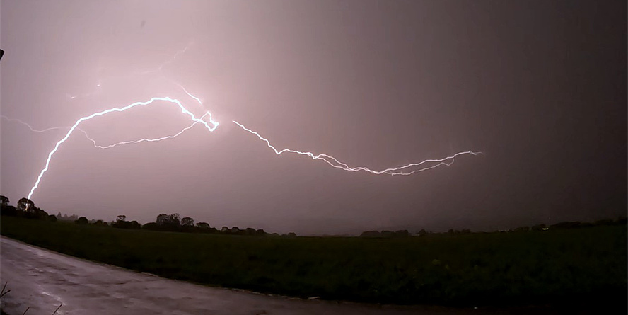 Ein Blitz entlädt sich aus einem wolkenverhangenen Himmel und schlägt in unbewohntem Gebiet ein.
