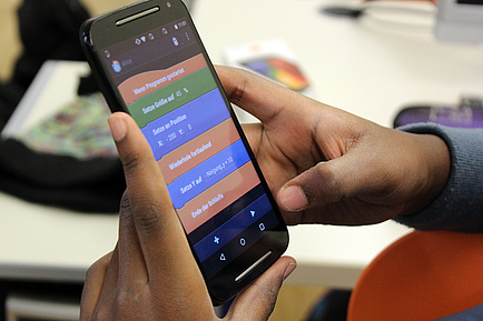 Ein Kind im Unterstufenalter hält ein Smartphone in Händen und programmiert 