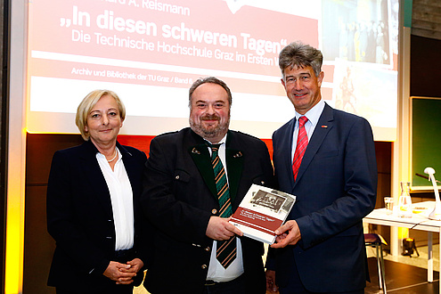 Die Leiterin des Verlages der TU Graz, Ulrike Krießmann, Autor und TU Graz-Archivar Bernhard A. Reismann sowie TU Graz-Rektor Harald Kainz stehen nebeneinander. Die Herren halten gemeinsam eine Ausgabe des Buches in Händen. 
