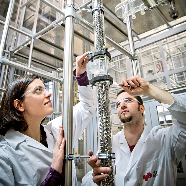 A woman and a man in lab clothes work on a pipe. 