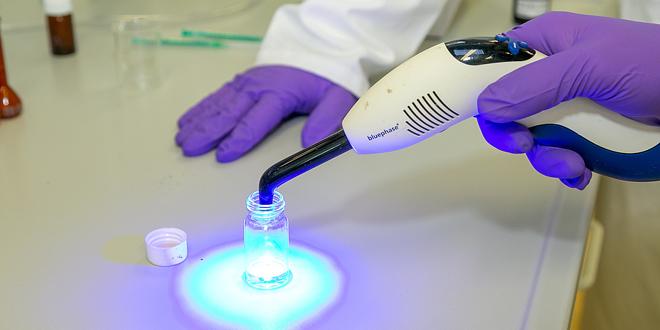 Nahaufnahme von Händen in Laborhandschuhen mit Lichtquelle.