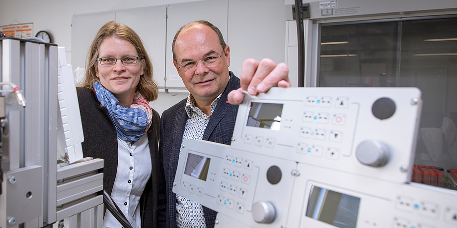 Eine Forscherin und ein Forscher stehen nehmen einem Laborgerät