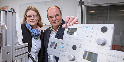 A female and a male researcher in a lab next to a laboratory apparatus